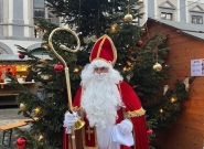 Nikolaus in rotem Gewand mit Bischofsstab und Geschenkbeutel vor einem geschmückten Weihnachtsbaum auf dem Adventmarkt in Schloss Kobersdorf.